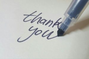 The tip of a pen writing the words "thank you"